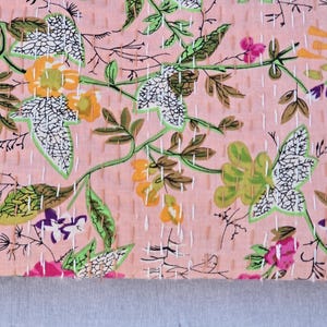 May include: A pink floral fabric with a repeating pattern of leaves and flowers in shades of green, yellow, purple, and pink. The design is stitched with white thread, creating a quilted effect. The bottom edge is a solid gray.