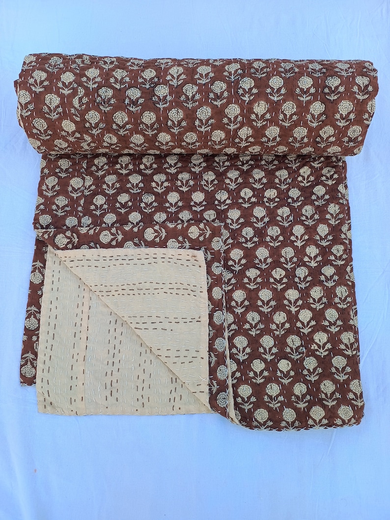 Puede incluir: Un edred&oacute;n marr&oacute;n enrollado con un estampado floral crema. El edred&oacute;n est&aacute; hecho de tela suave y presenta detalles cosidos a mano. La parte inferior es crema con costuras horizontales. Textil decorativo para el hogar.