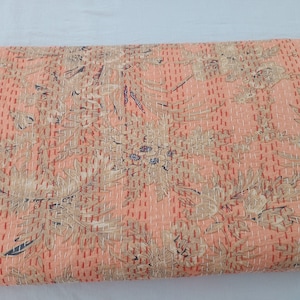 May include: A peach-colored quilt with a floral pattern in beige and navy blue. The quilt is covered in evenly spaced, vertical rows of red stitching. The floral design is a repeating pattern across the entire surface.
