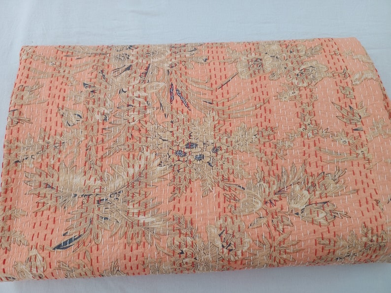 May include: A peach-colored quilt with a floral pattern in beige and navy blue. The quilt is covered in evenly spaced, vertical rows of red stitching. The floral design is a repeating pattern across the entire surface.