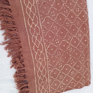 May include: A brown cotton throw blanket with a white geometric pattern and fringe on the edges.