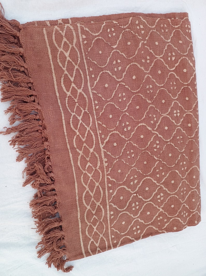 May include: A brown cotton throw blanket with a white geometric pattern and fringe on the edges.