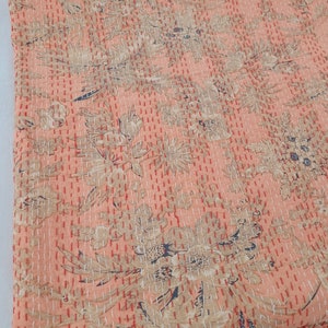 May include: A peach-colored textile with a floral pattern in beige and navy blue. The fabric is densely stitched with red thread, creating a quilted effect. The design features stylized flowers and foliage.