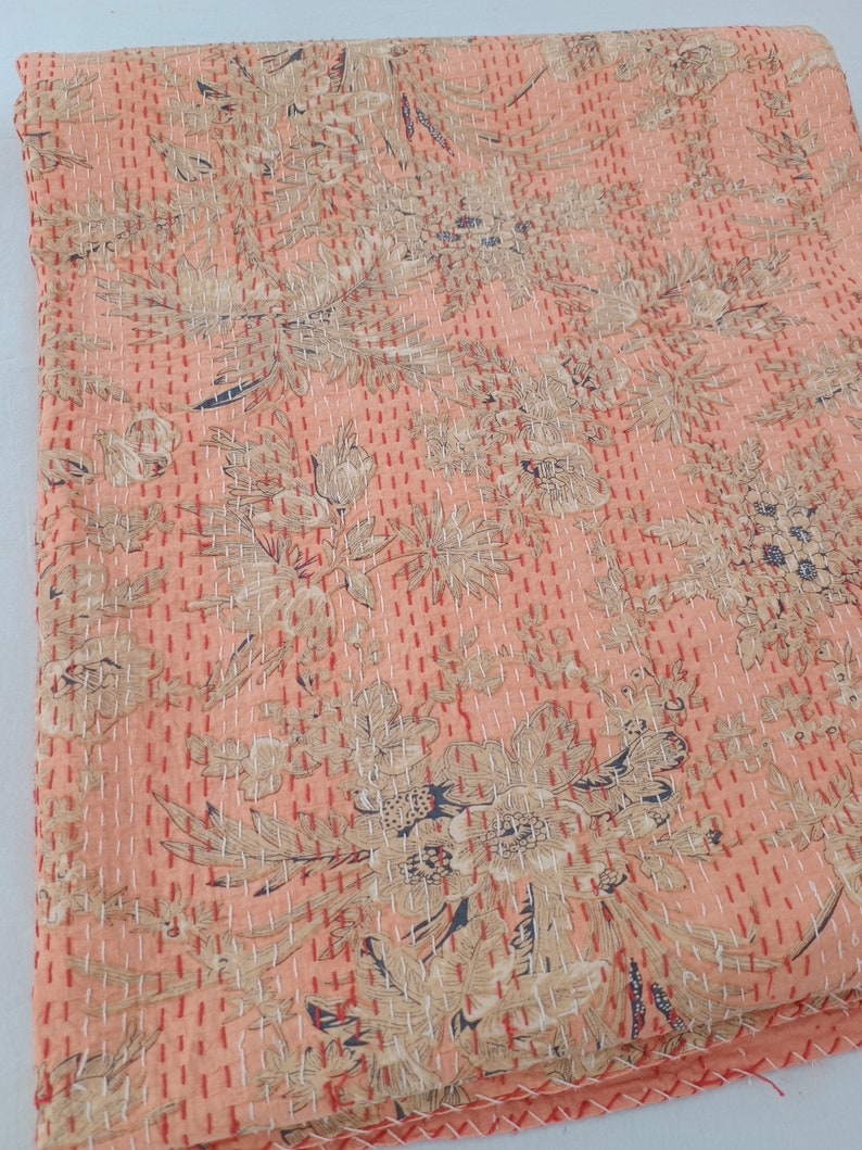 May include: A peach-colored textile with a floral pattern in beige and navy blue. The fabric is densely stitched with red thread, creating a quilted effect. The design features stylized flowers and foliage.