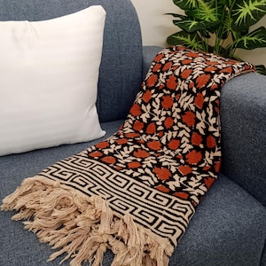 Może przedstawiać: Brązowo-czarny koc z kwiatowym wzorem i frędzlami. Koc leży na niebieskiej kanapie.