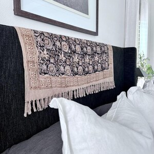 May include: A black headboard with a patterned throw pillow and a white throw pillow. The headboard is covered in a dark fabric with a tufted design. The throw pillows are made of a soft, white fabric.