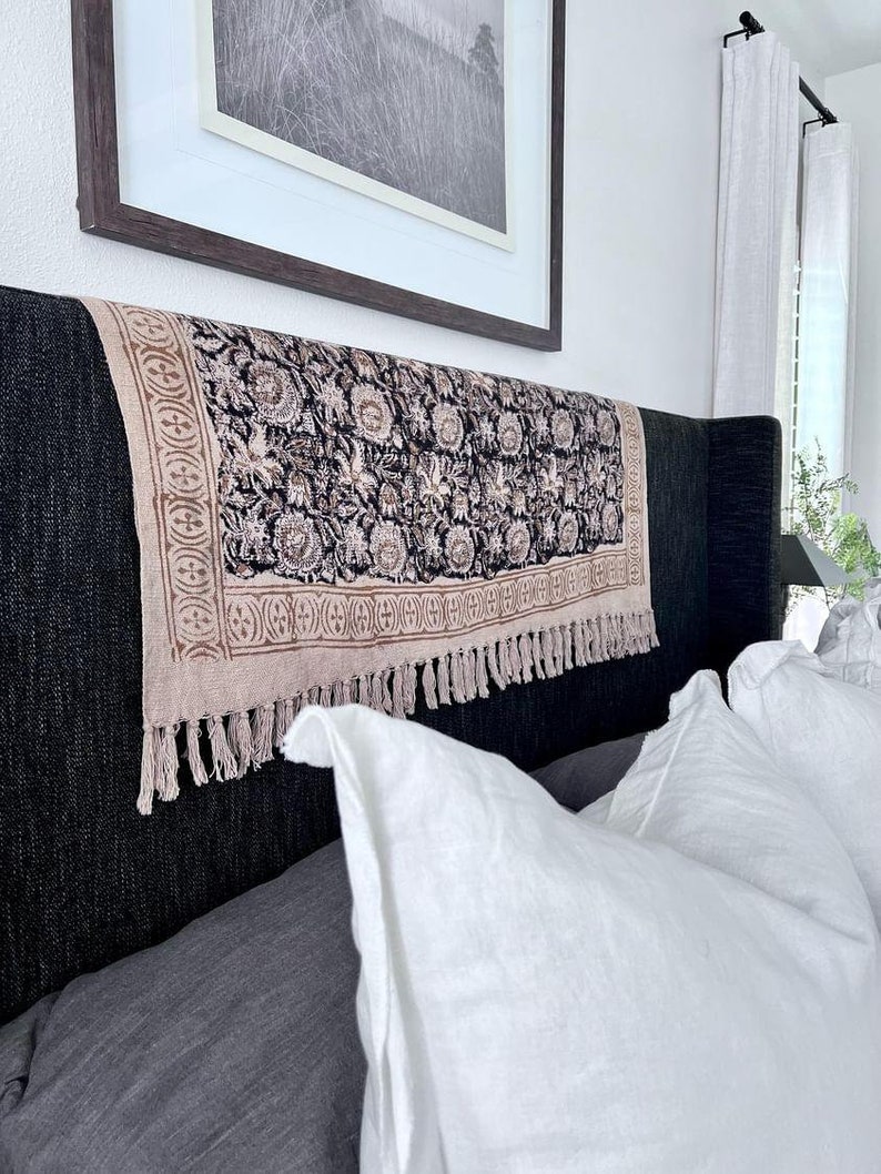 May include: A black headboard with a patterned throw pillow and a white throw pillow. The headboard is covered in a dark fabric with a tufted design. The throw pillows are made of a soft, white fabric.