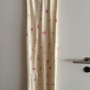 May include: A sleeveless maxi dress with a floral print. The dress is a light cream color with pink and purple flowers.