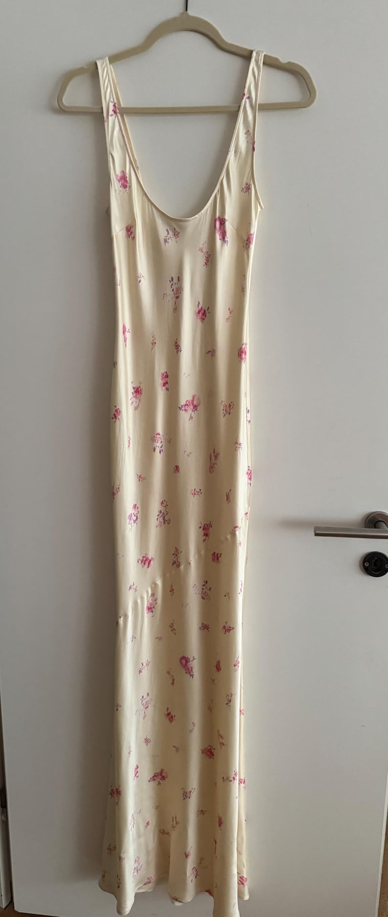 May include: A sleeveless maxi dress with a floral print. The dress is a light cream color with pink and purple flowers.