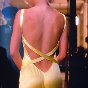 Puede incluir: Una mujer con un vestido de sat&eacute;n amarillo con la espalda descubierta y tirantes cruzados.