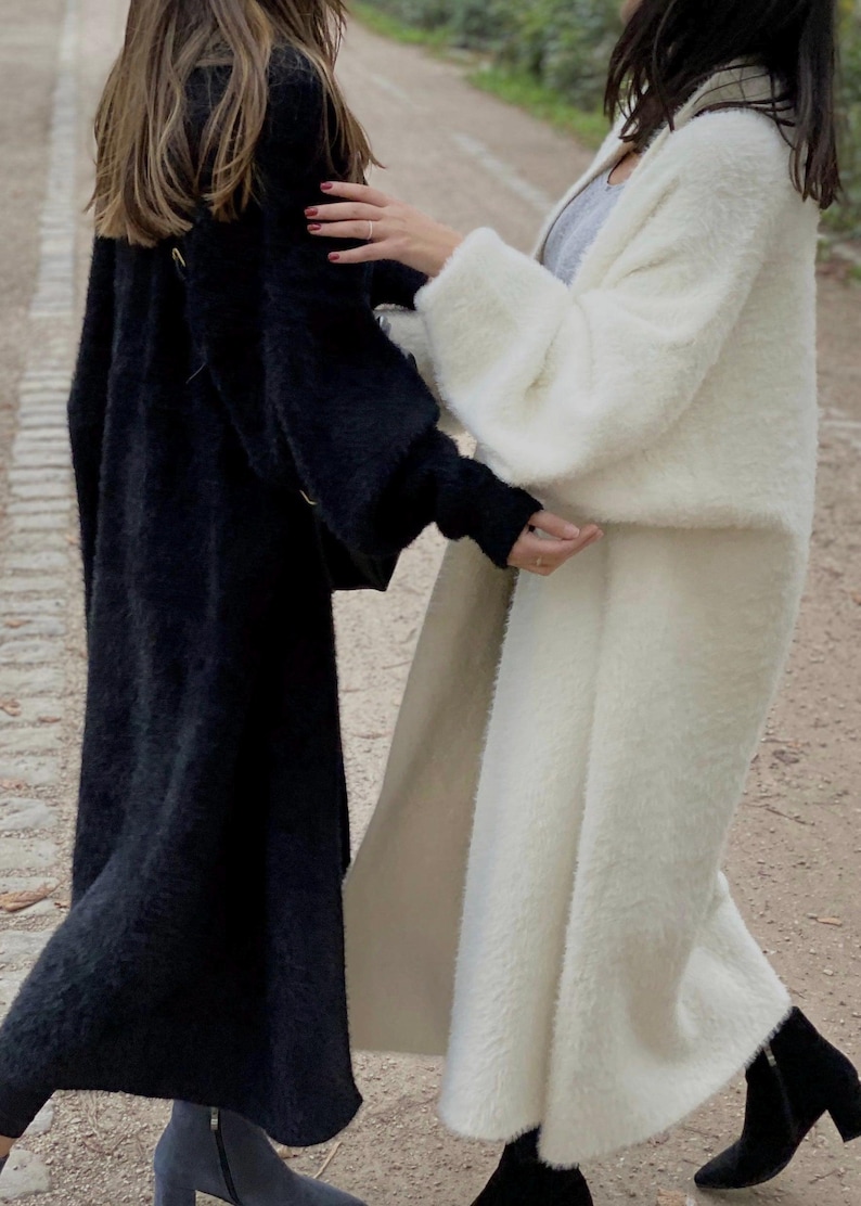 Op de afbeelding: Twee vrouwen dragen lange, pluche cardigans. E&eacute;n cardigan is zwart en de andere is wit.