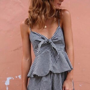 May include: A woman wearing a black and white gingham print top and shorts with a straw hat. The top has a bow at the front.