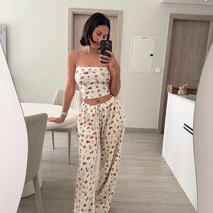 May include: A white crop top with a red and white cherry print and matching wide-leg pants.
