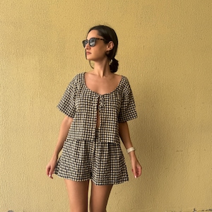 K&ouml;nnte beinhalten: Ein zweiteiliges Set bestehend aus einem kurz&auml;rmeligen Oberteil und passenden Shorts, beide mit einem schwarz-wei&szlig;en Vichy-Karo-Muster. Das Oberteil hat einen Rundhalsausschnitt mit einer Bindeschleife auf der Vorderseite.