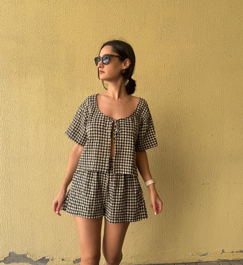 K&ouml;nnte beinhalten: Ein zweiteiliges Set bestehend aus einem kurz&auml;rmeligen Oberteil und passenden Shorts, beide mit einem schwarz-wei&szlig;en Vichy-Karo-Muster. Das Oberteil hat einen Rundhalsausschnitt mit einer Bindeschleife auf der Vorderseite.