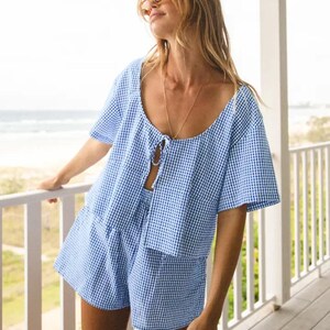 May include: A blue and white gingham patterned short-sleeved top and matching shorts. The top has a tie at the front and the shorts have a high waist.