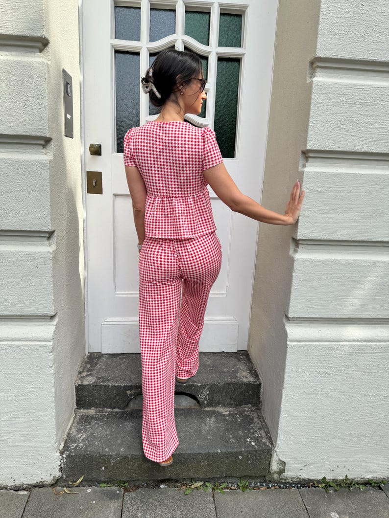 May include: A two-piece set consisting of a short-sleeved peplum top and matching wide-leg trousers, both featuring a red and white gingham check pattern. The top has a fitted bodice with a flared waist, and the trousers have a straight-leg cut.
