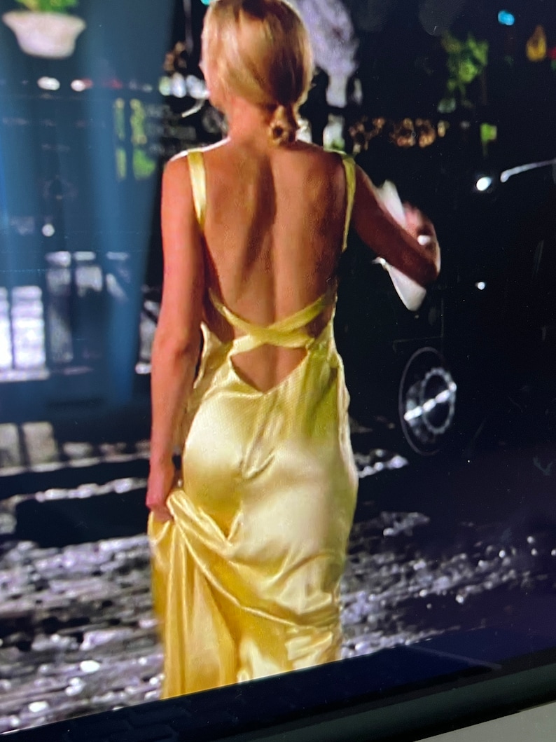 Puede incluir: Una mujer con un vestido de sat&eacute;n amarillo con la espalda baja y un dise&ntilde;o de tirantes cruzados.