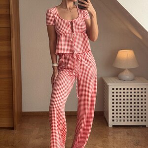 May include: A two-piece set consisting of a short-sleeved top and wide-leg trousers, both featuring a red and white gingham check pattern. The top has a scoop neckline with a front tie closure, and the trousers include an adjustable drawstring waist.