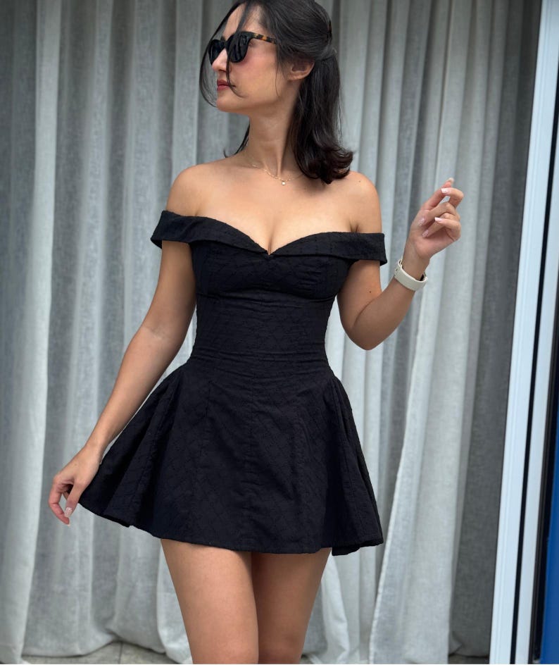 May include: A black off-the-shoulder dress with a fitted bodice and flared skirt. The dress has a textured pattern and is worn with sunglasses.