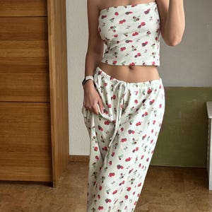 May include: A white strapless top and matching pants with a small red and white floral print. The top is cropped and the pants are wide-legged.