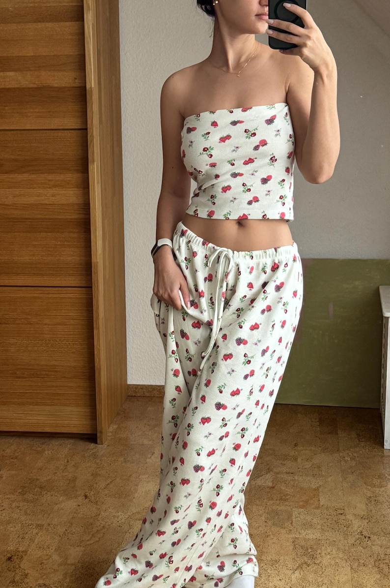 May include: A white strapless top and matching pants with a small red and white floral print. The top is cropped and the pants are wide-legged.