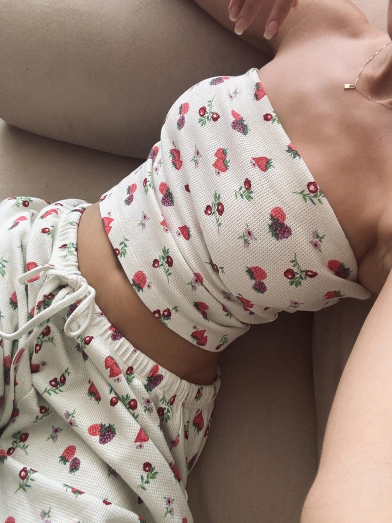 May include: A white pajama set with a strawberry print. The top is a strapless tube top and the bottoms are pants with a drawstring waist.