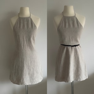 May include: A beige linen halter dress with a black belt. The dress is sleeveless and has a straight neckline. It is shown on a white background.