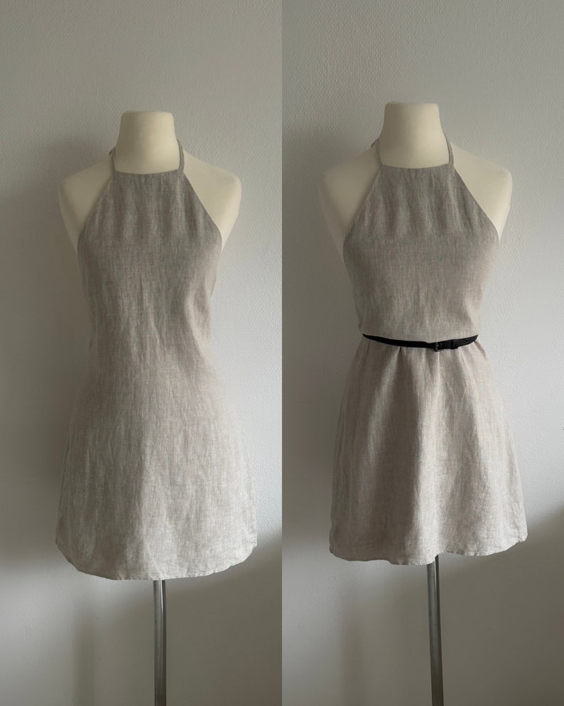 May include: A beige linen halter dress with a black belt. The dress is sleeveless and has a straight neckline. It is shown on a white background.