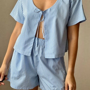 May include: A blue and white gingham pajama set with a short-sleeved top that ties at the front and matching shorts.