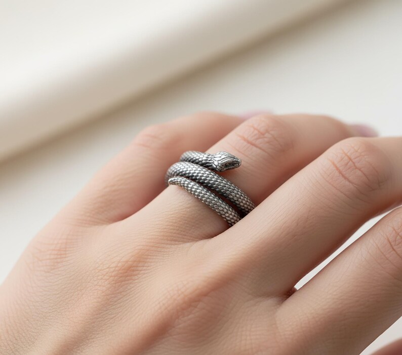 A close-up image of a person's hand wearing a silver ring with a snake design.