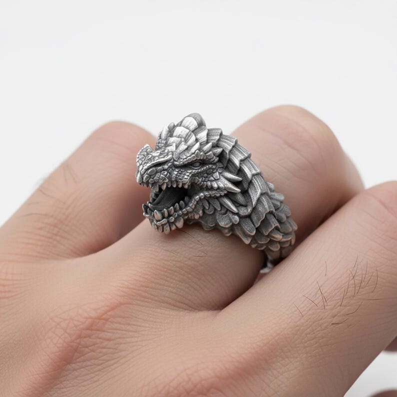A close-up image of a person's hand wearing a ring featuring a detailed, metallic dragon head design.