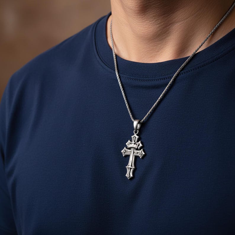 A silver cross pendant is worn on a person's neck, set against a navy blue shirt.
