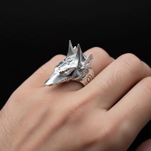 A close-up image of a person's hand wearing a silver ring in the shape of a fox's head.