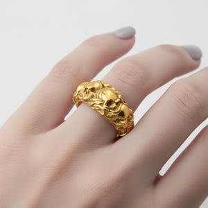A close-up of a gold ring with a skull design on the finger.