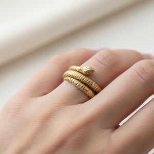 A close-up image of a person's hand wearing a gold snake-shaped ring on the ring finger.