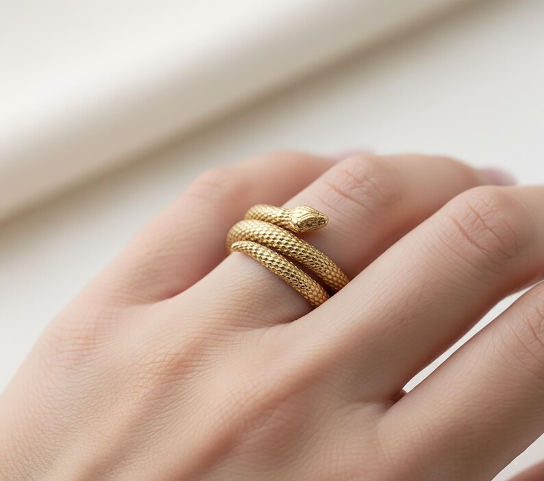 A close-up image of a person's hand wearing a gold snake-shaped ring on the ring finger.