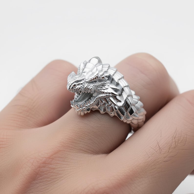 A close-up image of a person's hand wearing a silver dragon head ring.