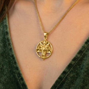 A gold-colored pendant necklace with an intricate design is worn around a person's neck.