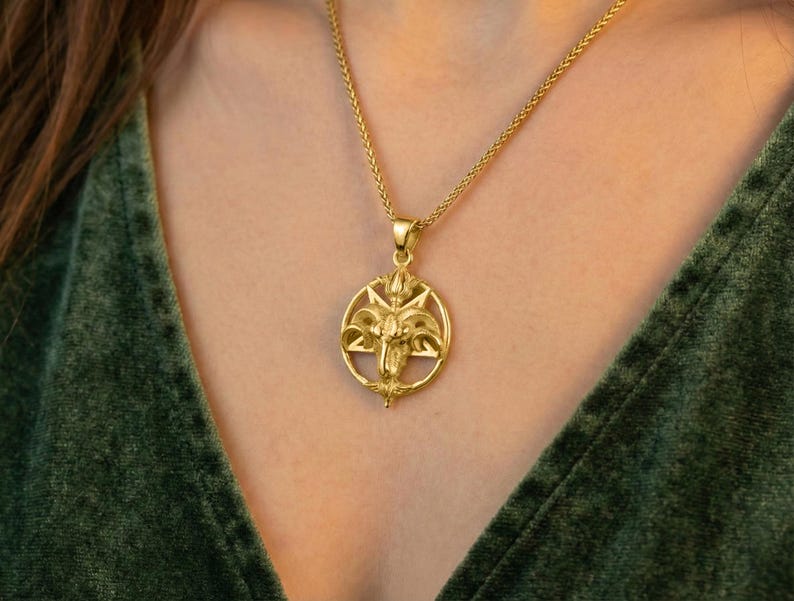 A gold-colored pendant necklace with an intricate design is worn around a person's neck.