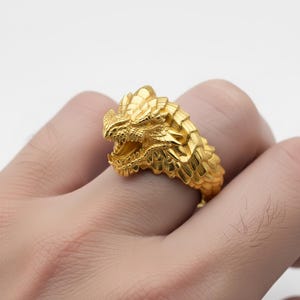 A close-up image of a person's hand wearing a gold dragon head ring.