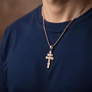 A gold cross pendant is worn on a person's neck, set against a navy blue shirt.