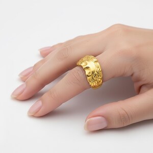 A close-up of a hand wearing a gold ring with an intricate design.