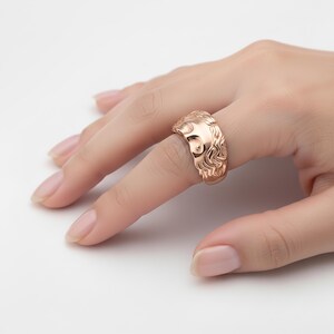 A close-up of a person's hand wearing a gold ring with an intricate design.