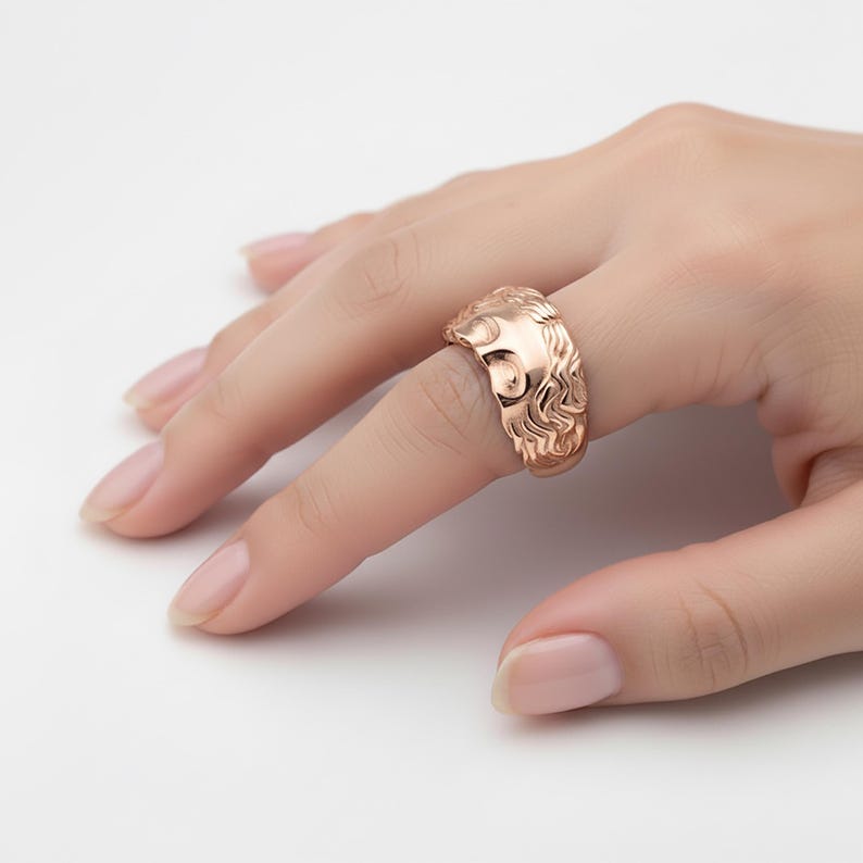 A close-up of a person's hand wearing a gold ring with an intricate design.