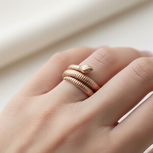 A close-up image of a person's hand wearing a gold-colored snake-shaped ring on the ring finger.