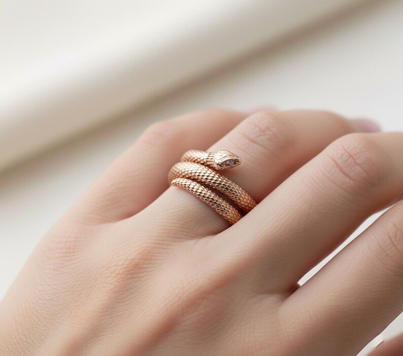 A close-up image of a person's hand wearing a gold-colored snake-shaped ring on the ring finger.