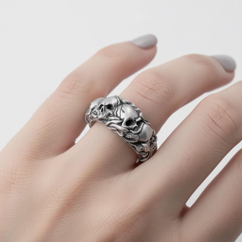 A close-up of a person's hand wearing a silver ring with an intricate design featuring multiple skulls.