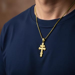 A gold cross pendant is worn by a person in a navy blue shirt.