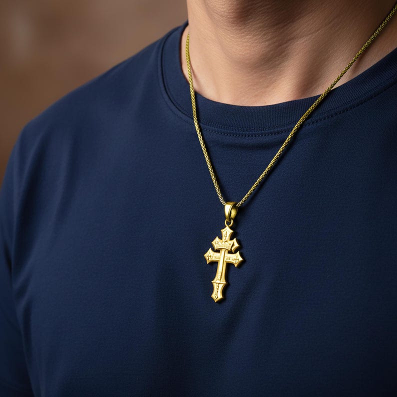 A gold cross pendant is worn by a person in a navy blue shirt.